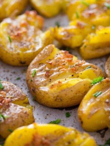 fingerling smashed potatoes sprinkled with chives on a baking sheet.